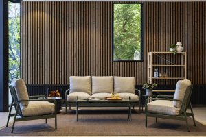 Interieurfoto met WoodUpp-producten: een driepersoons loungebank en twee bijpassende fauteuils met olijfgroene metalen frames en beige kussenbekleding, een lage salontafel met glazen blad en een open houten wandkast naast de verticale WoodUpp lamellenwand. Planten en accessoires benadrukken de warme, natuurlijke sfeer.