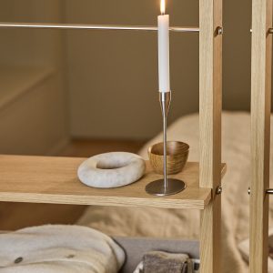 WoodUpp eikenhouten roomdivider met slanke horizontale planken en roestvrijstalen stangen, zichtbaar als open scheidingsrek. Op het plankje staan een slanke metalen kandelaar met brandende kaars, een klein houten kommetje en een rond marmeren decorstuk. Planken tonen warme, natuurlijke eikenafwerking en zichtbare metalen verbindingsbouten.