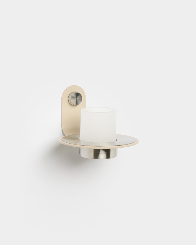 WoodUpp wandkandelaar met beige metalen bevestigingsplaat, verzonken roestvrijstalen theelichthouder en ronde matte metalen schijf; in het midden een gesatineerd wit cilindrisch glas voor een kaars. Aan de plaat een decoratieve, geribbelde draaiknop; elegant en compact, ideaal voor stijlvolle hal of slaapkamer.